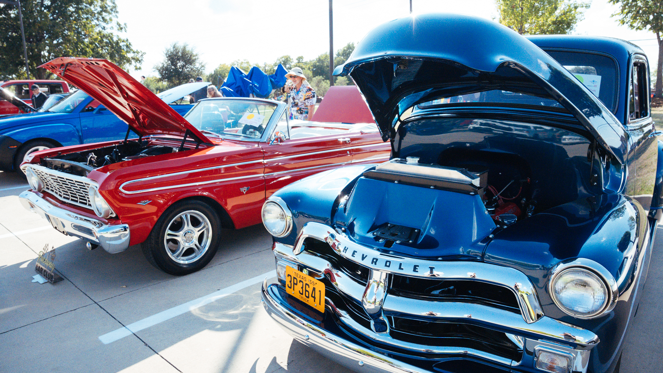 Vintage cars with hoods open for car show. One red mustang and one dark Chevrolet truck 